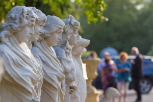 Five Cast stone sculptures of women in a row with people talking in the far background