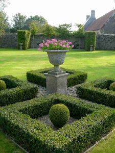 A formal garden with box hedging with a large planted urn on a pedestal to add floral interest and colour.
