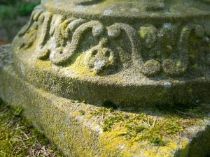 Close up of weathered old cast stone garden ornament with moss and lichen