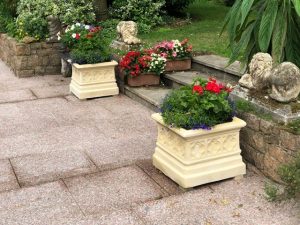 A garden path with a pair of matching garden planters either side of the entrance , planted with summer bedding plants. 