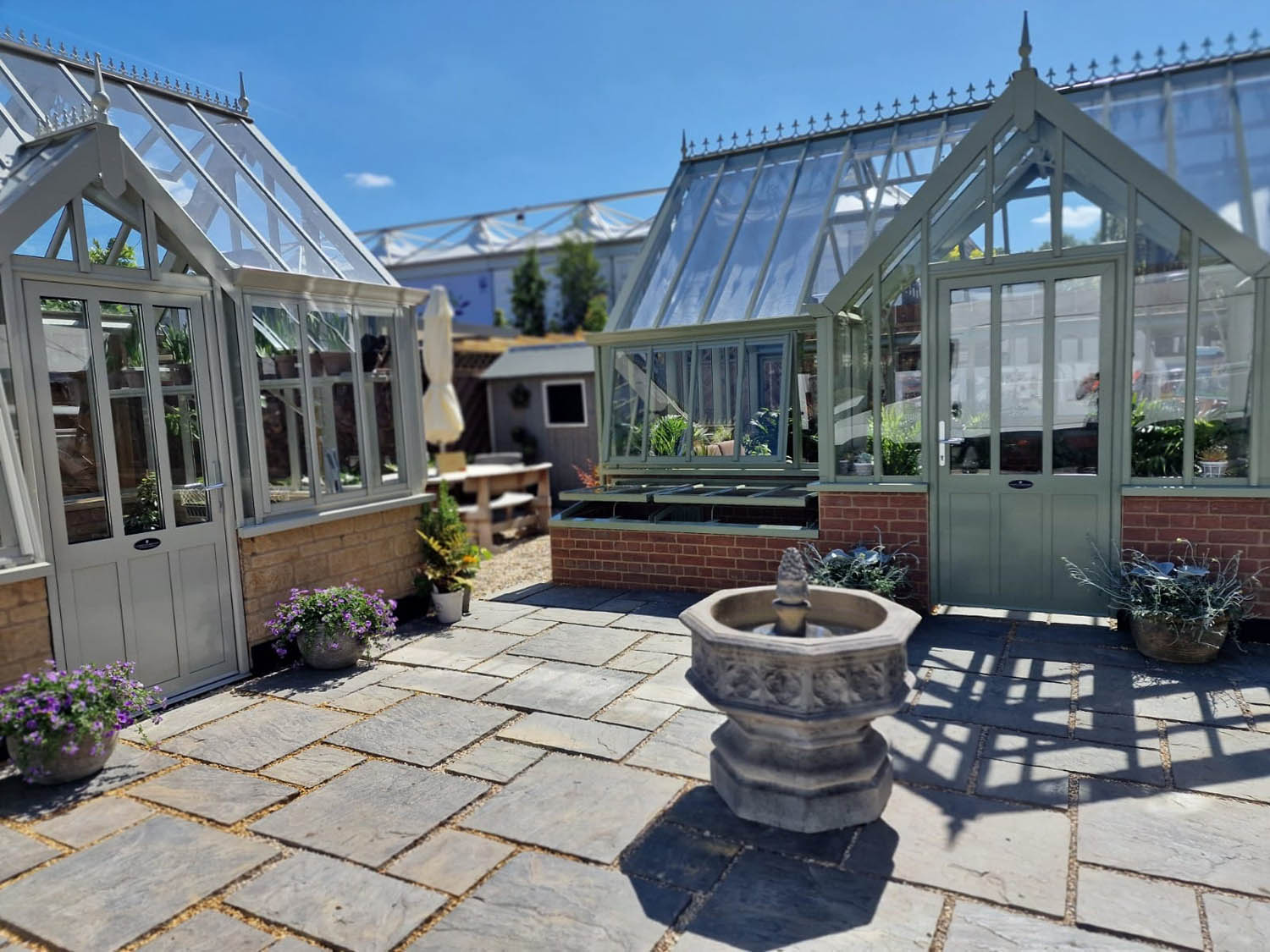 Traditional stone fountain and glass houses create a patio garden style stand at RHS Chelsea flower show 2022 with Griffin glasshouse and Chilstone