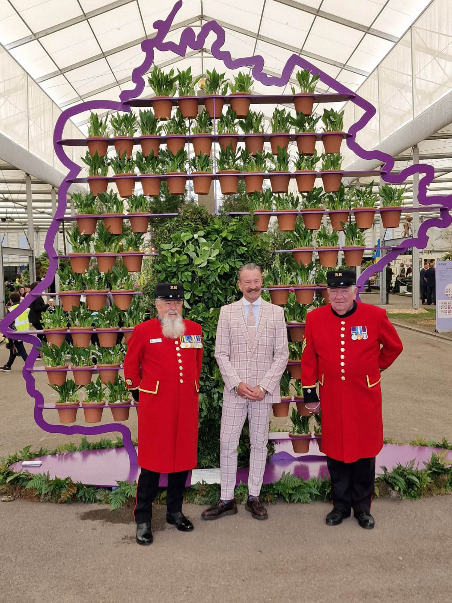 Chelsea pensioners in red uniform stand with Simon Lycett garden designer in front of his amazing 3D silhouette portrait of the Queen made from foliage and 70 pots of HRM favourite flower Lilly of the valley representing 70 years on the thrown as part of the jubilee celebrations in the gardens