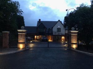 Image shows smart gate posts, topped with handmade Chilstone gate pier capitals and ball finials, illuminated with stylish uplighters to create a smart and impressive property entrance