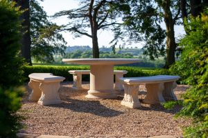 A garden with three stone benches around a large, round stone garden table with a holiday feel. 