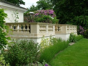 A garden patio edged in classic baluster style cast stone balustrading, topped with coping stones for a polished finish in an traditional country garden design.