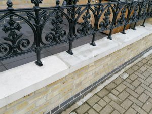A low front garden wall topped with sleek coping stones and Victorian style black railings.